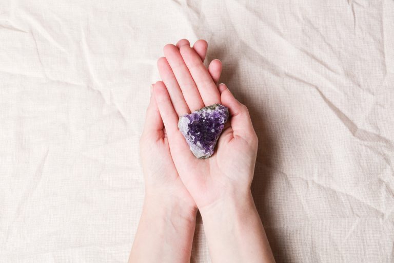 druse raw purple amethyst crystal on piece of stone on woman hand on grey linen, magic rock for ritu