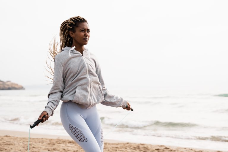Fit african woman jumping rope doing workout routine at the beach - Focus on face
