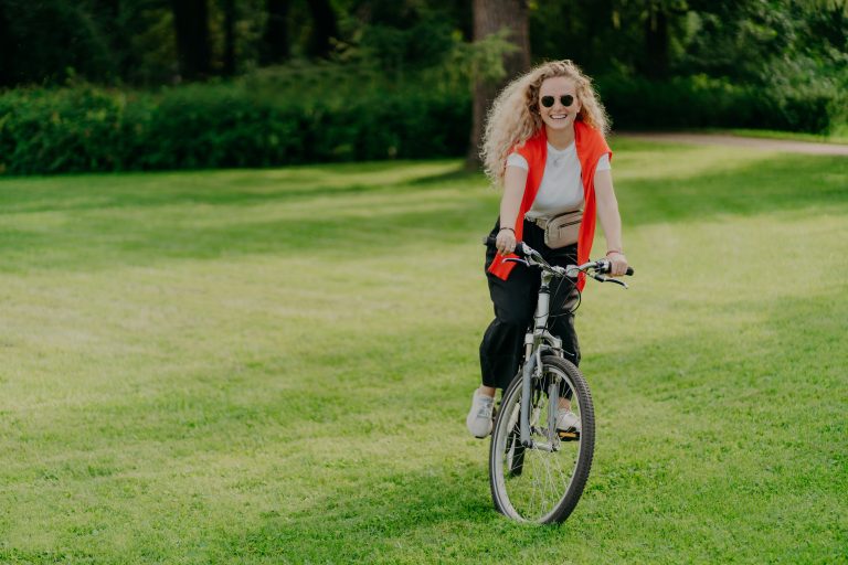 Pretty woman rides bike, poses on green lawn, spends free time in park, bikes in beautiful nature