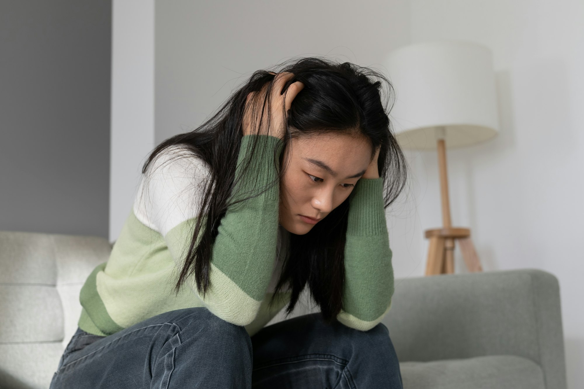 Anxious worried Asian millennial girl holding head in hands dealing with depression after abortion