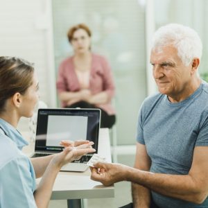 Caring Nurse Talking To Senior Man At Hospital Waiting Room