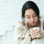 Young woman sick with temperature drinks hot