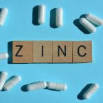 zinc, word in 3D wooden alphabet letters surrounded by white zinc pill capsules isolated on blue bac