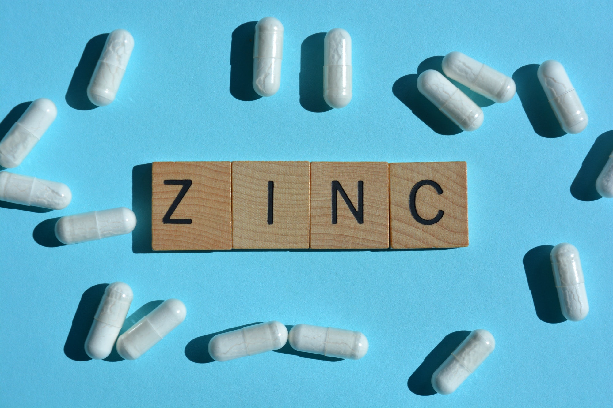 zinc, word in 3D wooden alphabet letters surrounded by white zinc pill capsules isolated on blue bac